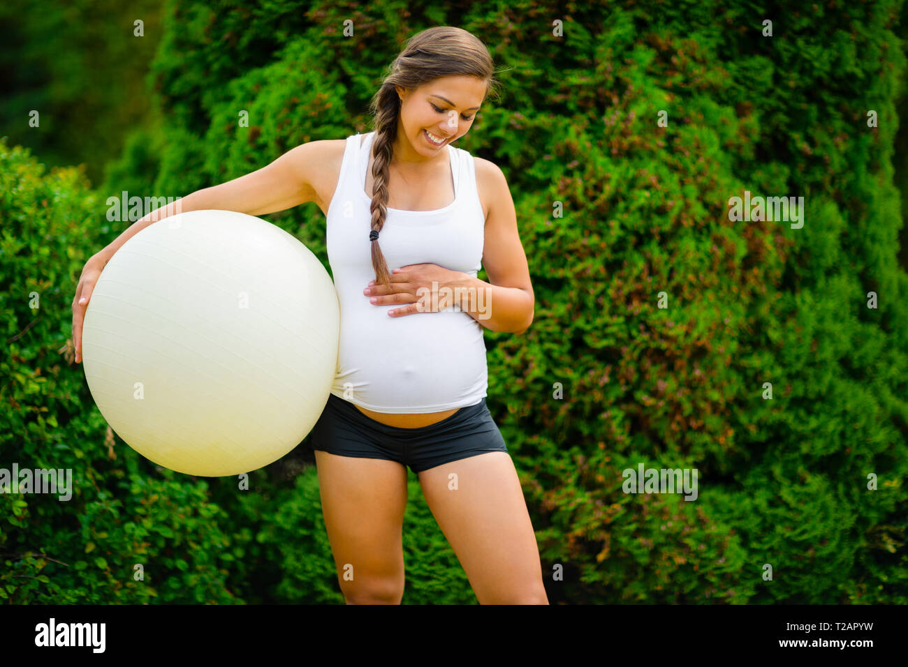 Sorridente femmine gravide toccando ventre tenendo palla Fitness Foto Stock