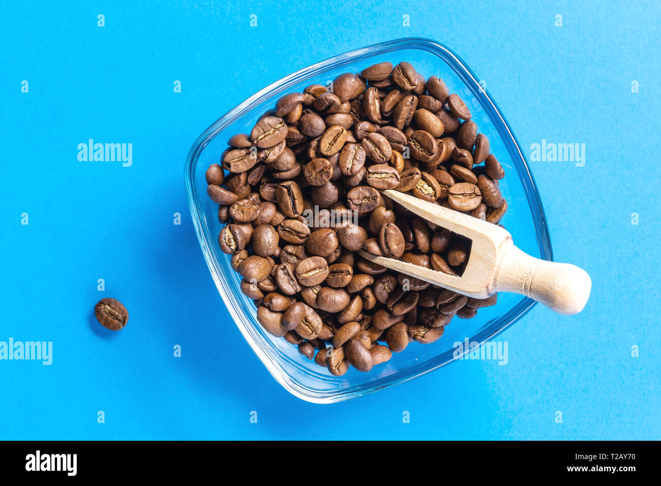 I chicchi di caffè nella ciotola con il cucchiaio di legno su sfondo blu Foto Stock