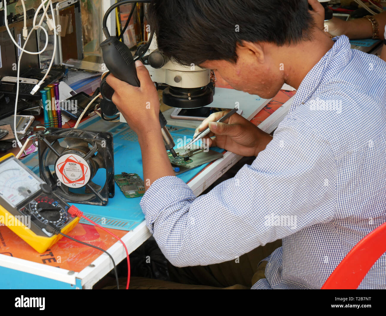 Un tecnico di Khmer la riparazione di un telefono mobile in corrispondenza di strada in una vetrina aperta shop in una città cambogiane. Battambang, Cambogia 13-12-2018 Foto Stock