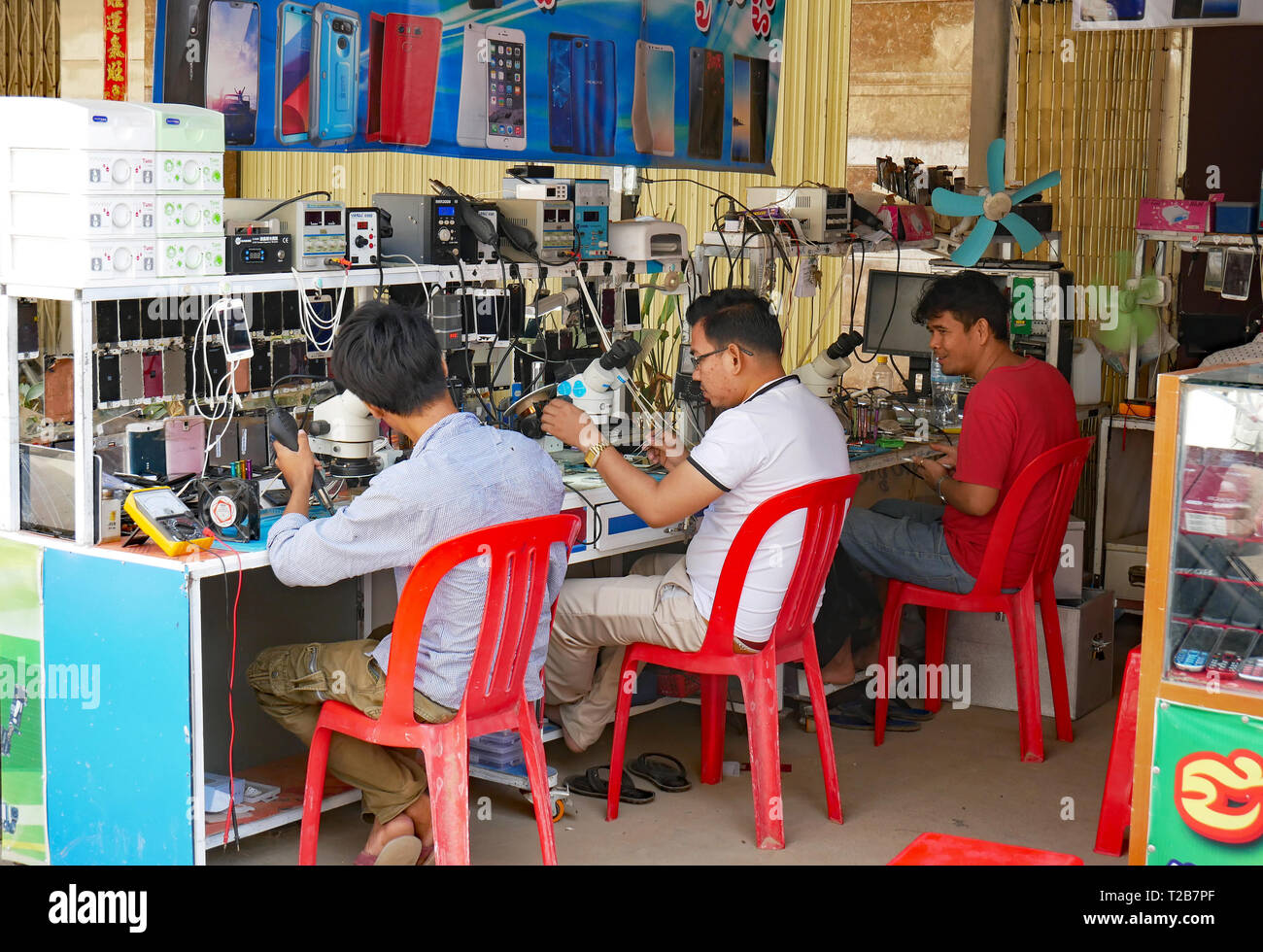 I tecnici di riparazione telefoni mobili su strada in un aperto fronteggiata shop in un cambogiano città mercato. Battambang, Cambogia 13-12-2018 Foto Stock