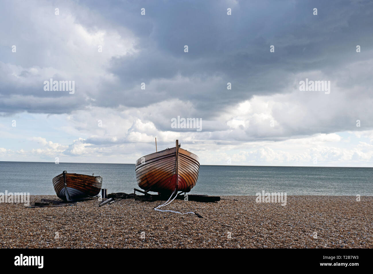 In prossimità di due piccole barche di legno su una spiaggia di ciottoli con il blu del mare acqua dietro e un drammatico sfondo con cielo nuvoloso Foto Stock
