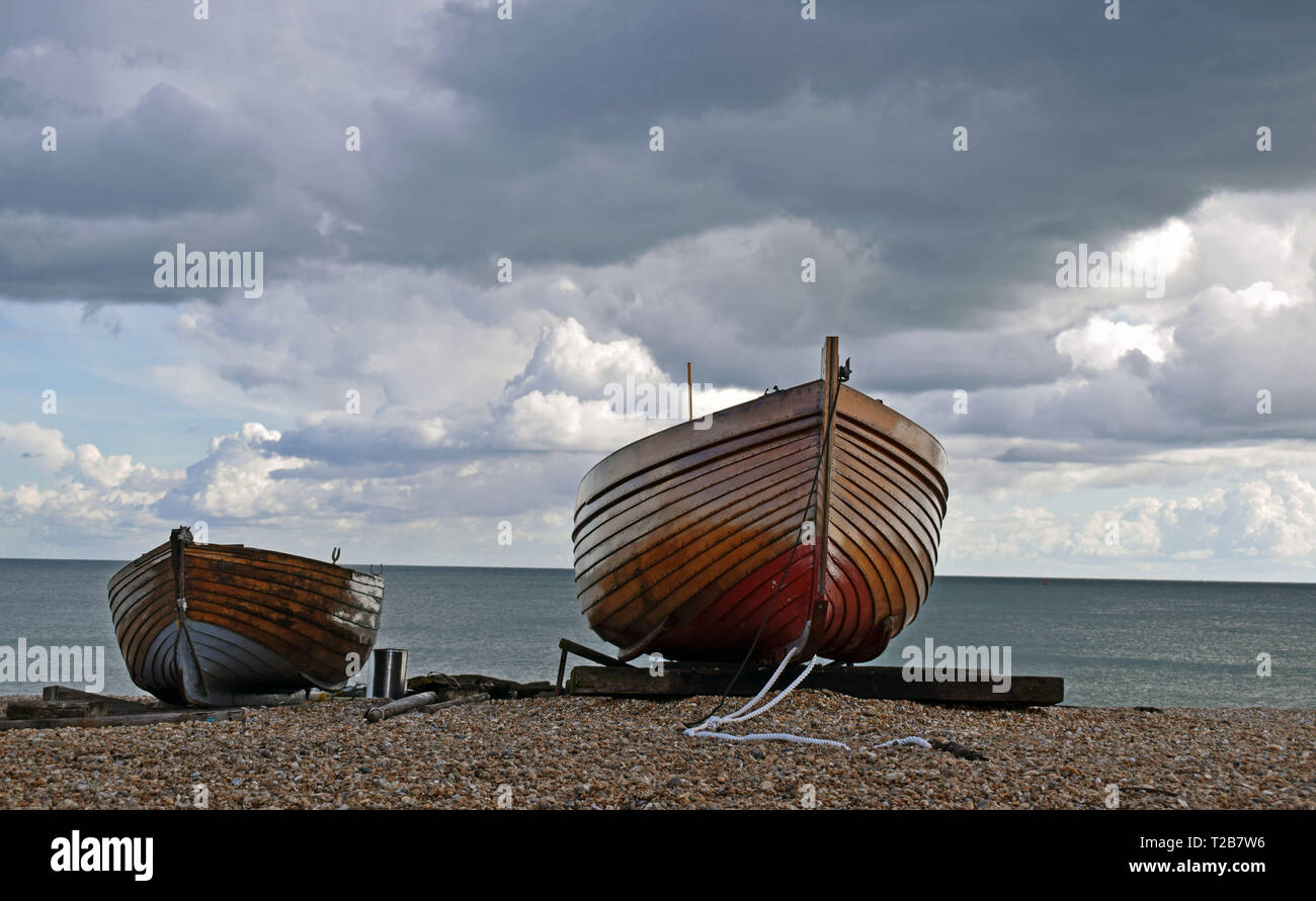 In prossimità di due piccole barche di legno su una spiaggia di ciottoli con il blu del mare acqua dietro e un drammatico sfondo con cielo nuvoloso Foto Stock