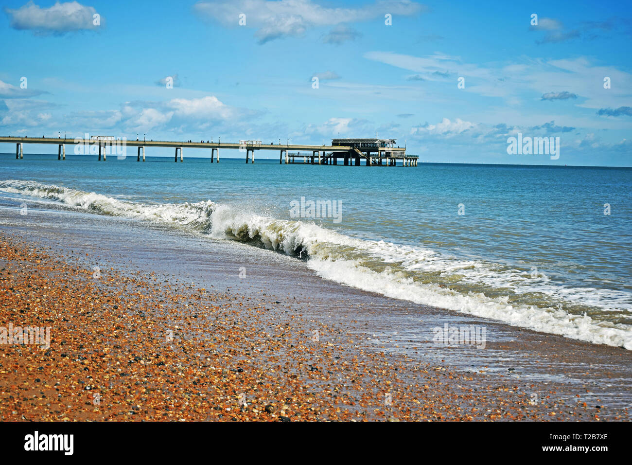 Mare di scena a trattare in Kent England con le onde provenienti sulla spiaggia di ciottoli e il molo che si allunga nel mare blu acqua con un cielo nuvoloso sopra Foto Stock
