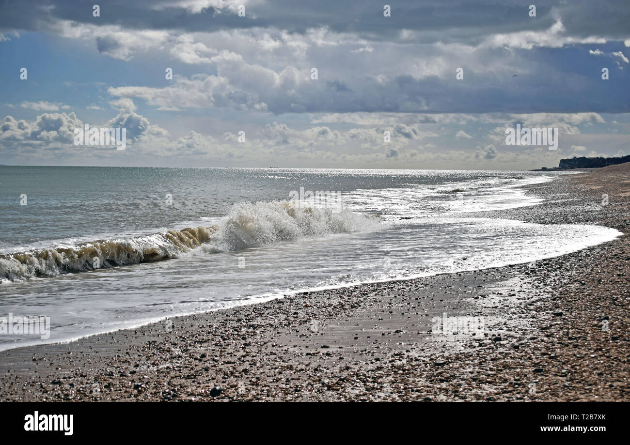 Bella vista sul mare di grezzo di onde che si infrangono sulla spiaggia di ciottoli con un drammatico cielo nuvoloso lungo la costa del Kent Foto Stock