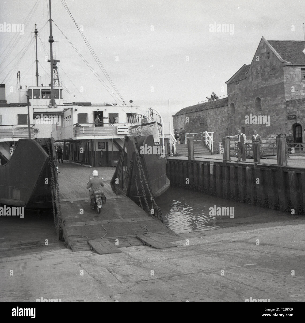 Degli anni Cinquanta, storico, un motociclista di salire a bordo di un vapore alimentato ferry ormeggiata in un porto, Inghilterra. Foto Stock