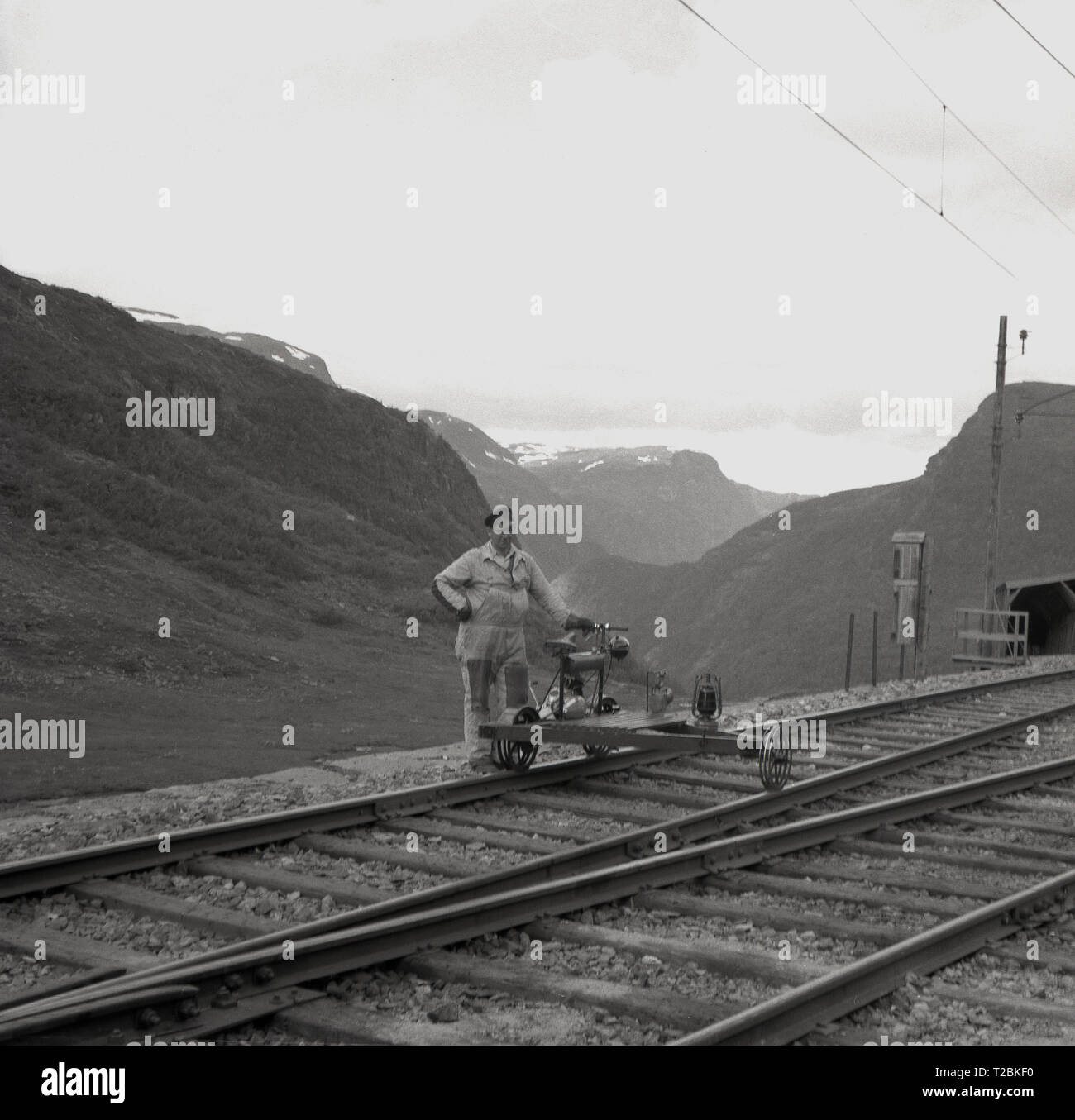 Degli anni Cinquanta, storico, operaio ferroviario in piedi su un binario ferroviario con una draisina o quello che è chiamato anche railbike, una speciale bicicletta adatta per l'uso su binari ferroviari, Norvegia. Questa luce ausiliaria veicolo ferroviario è utilizzato dal personale di servizio di trasporto e di equipaggio e materila necessari per la manutenzione dell'infrastruttura ferroviaria. Questo draisina sembra un piccolo motore a benzina attaccata al suo telaio. Foto Stock