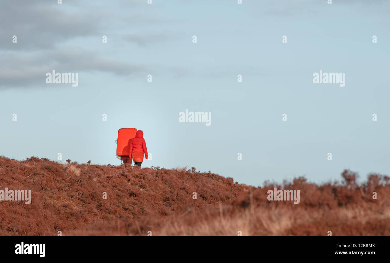 Due backpackers in arancio brillante vestiti contro la luce blue sky travel lungo il Peak District, UK - Primavera 2019 Foto Stock