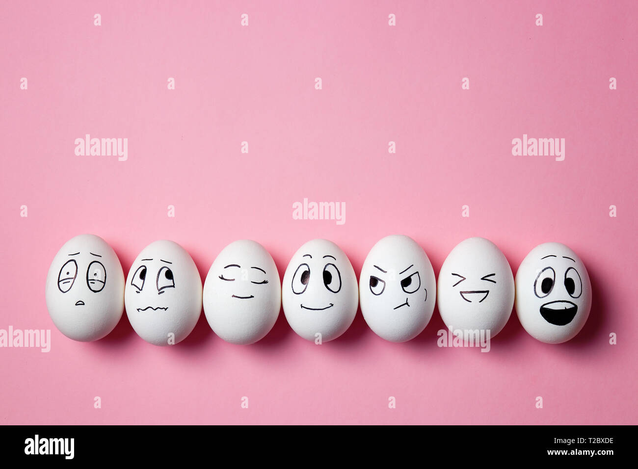 Divertenti le uova di pasqua con le espressioni del viso. Uova con facce diverse su sfondo rosa. Foto Stock