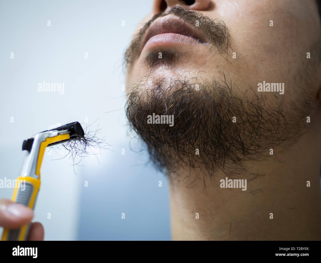 Closeup uomo utilizzare giallo rasoio disordinato di rasatura barba e baffi  sul suo volto nella stanza da bagno Foto stock - Alamy
