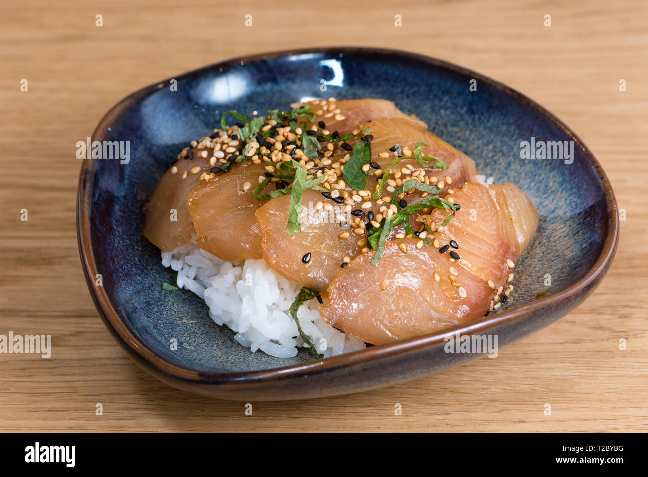 Ciotola con il salmone sashimi condito con in bianco e nero di sesamo, rucola, nori alghe fritte su un letto di il riso bianco cotto a vapore, tavolo in legno sfondo Foto Stock