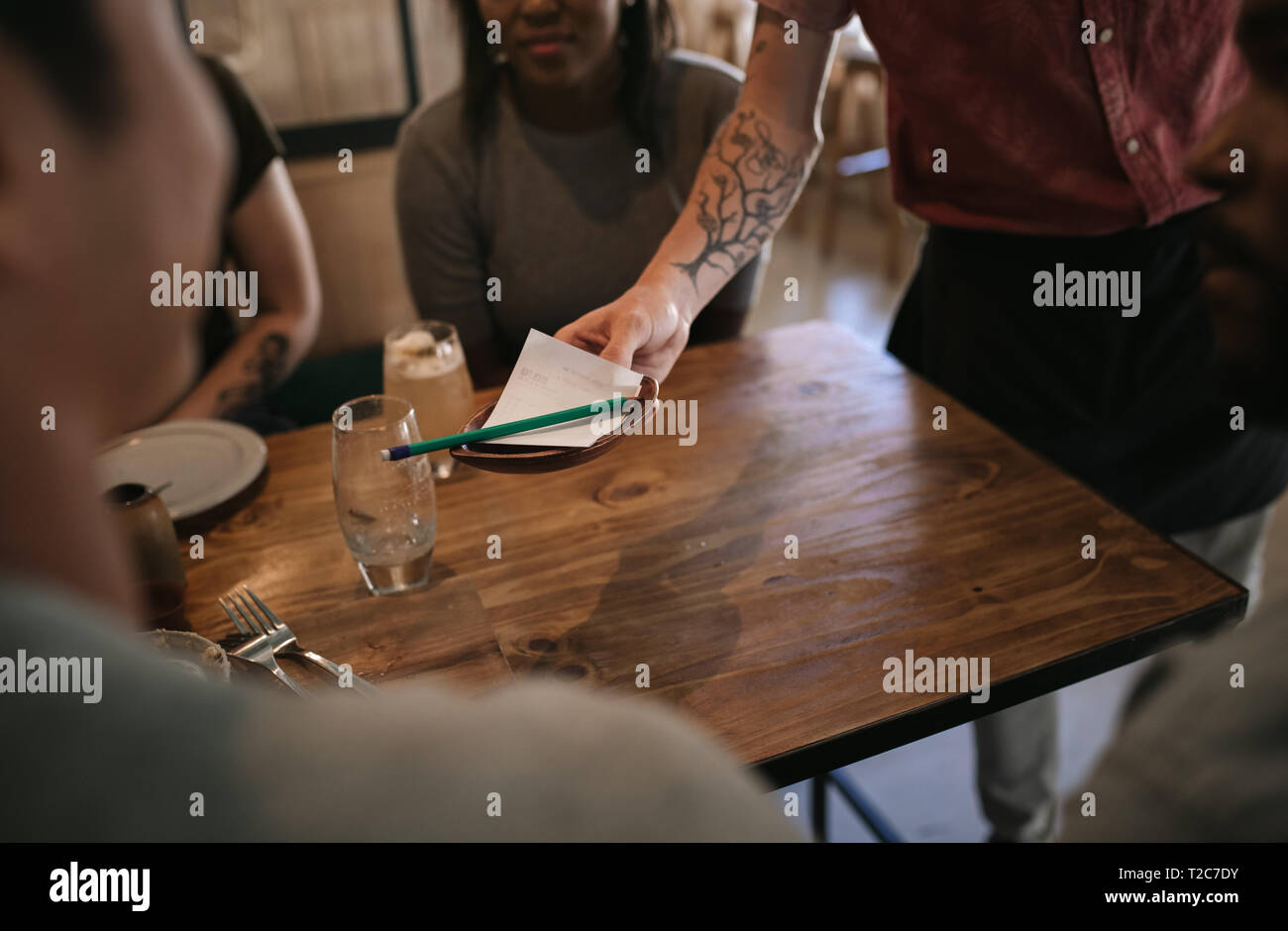 Cameriere consegna a un cliente il disegno di legge per la cena e per i drink dopo una notte fuori con gli amici in un bar Foto Stock