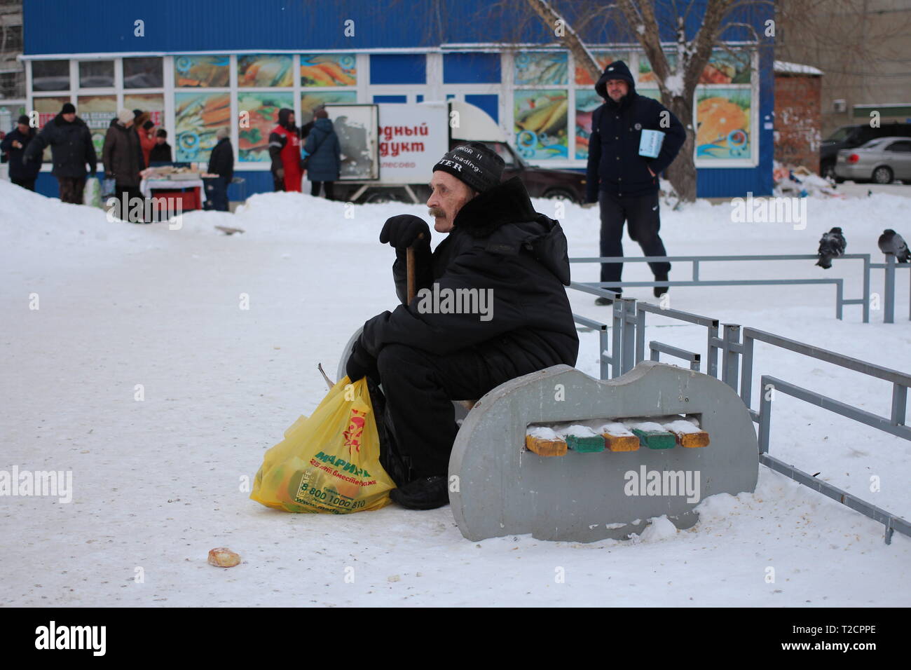 Il vecchio uomo malato pensionato uomo stanco seduta su una panchina in inverno vicino al negozio in città Foto Stock