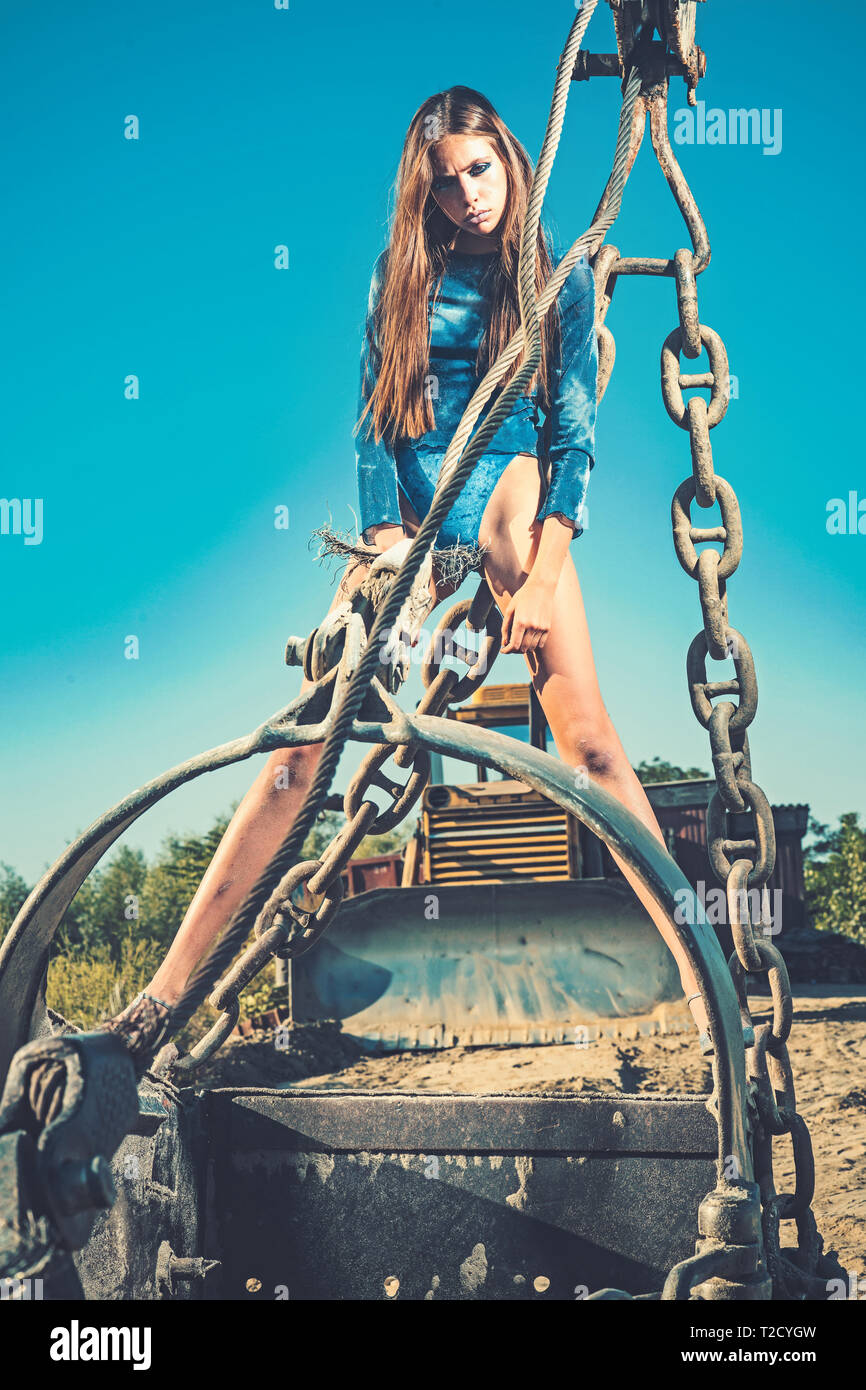 Donna in grande escavatore benna del cielo blu, industria. Donna con capelli lunghi in coppe nella pala, moda. Industria, attrezzature, macchina. Moda e bellezza Foto Stock