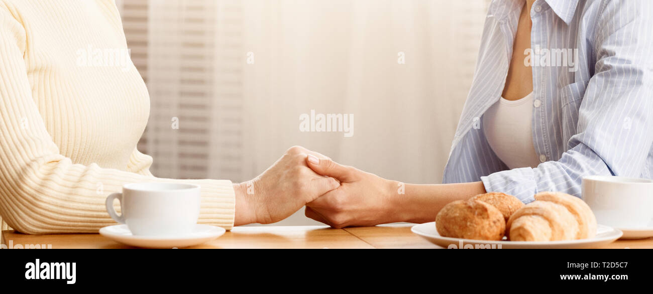 Figlia di madre tenendo la mano, mostrando la sua cura e supporto, avente la colazione a casa Foto Stock