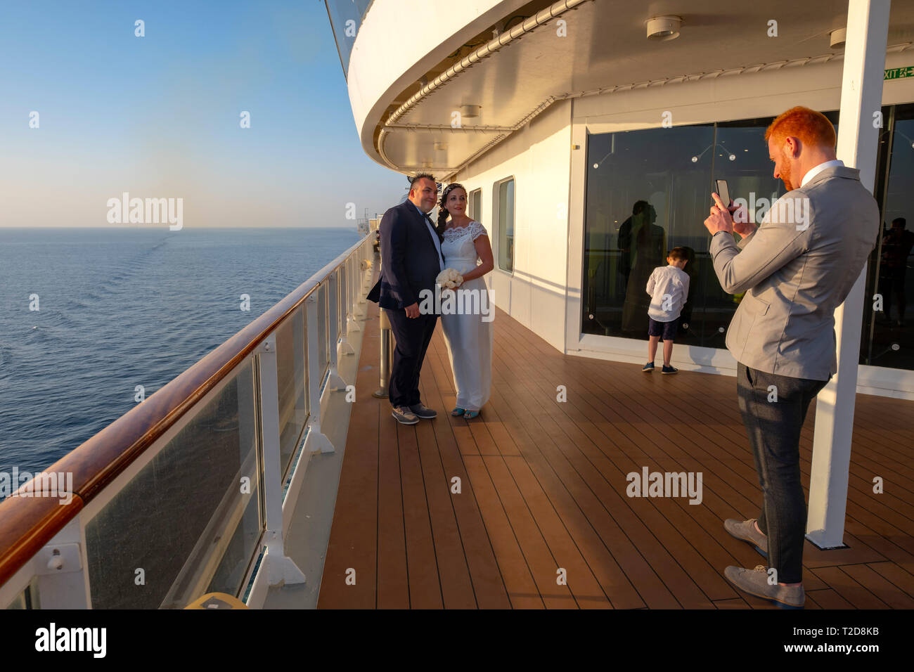 Uomo di scattare le foto di una sposa e lo sposo con il suo smartphone mentre sul ponte di una nave da crociera nave Foto Stock