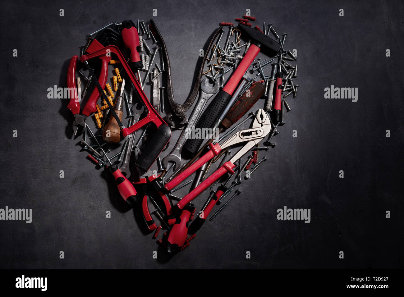 Lay piatto a forma di cuore ancora la vita della famiglia di strumenti per il fai da te con colorati manici rossi su sfondo grigio scuro con spazio di copia Foto Stock