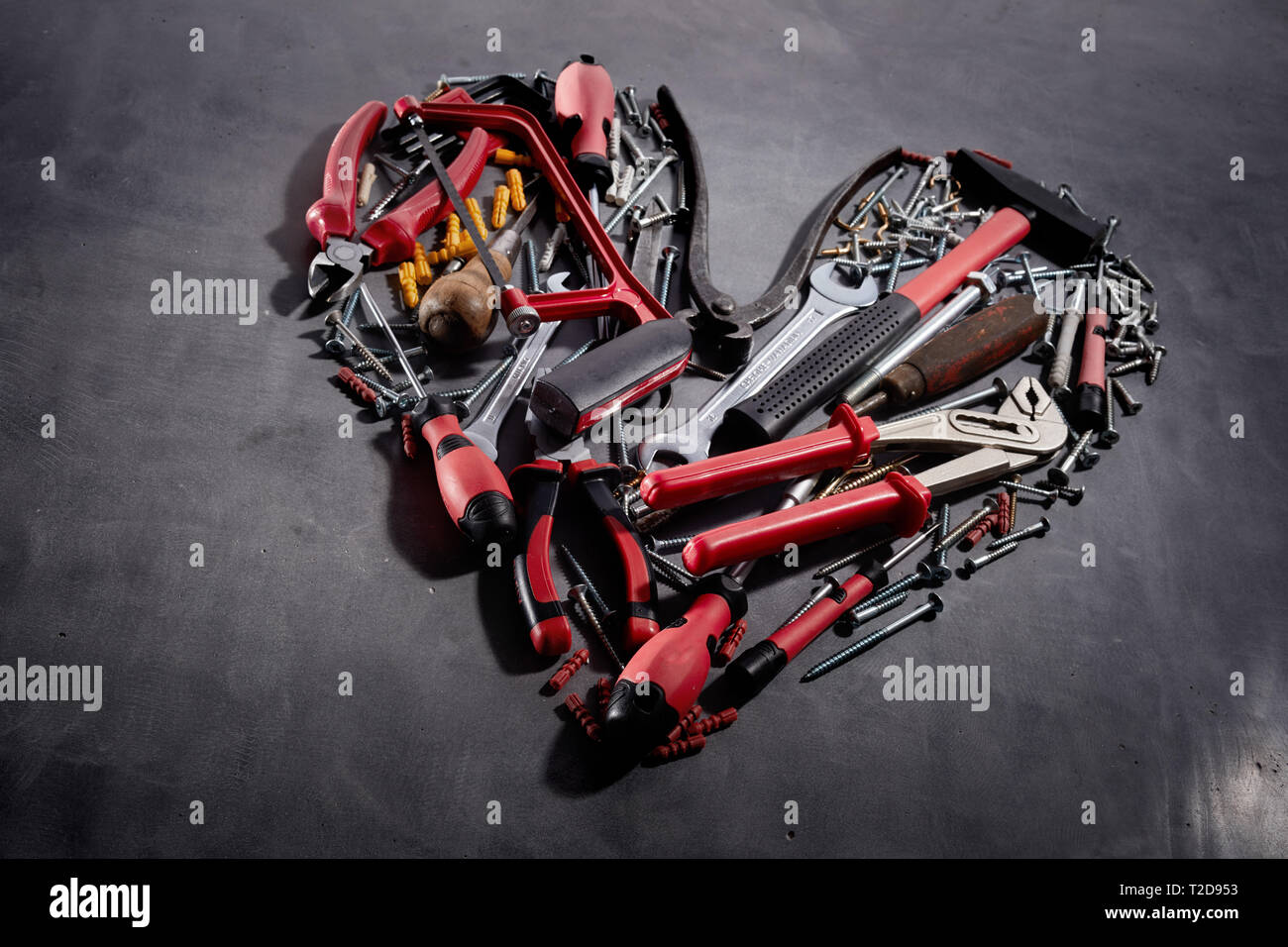 A forma di cuore ad disposizione degli attrezzi di mano assortiti e viti visto obliquamente su una superficie strutturata sfondo grigio scuro in un concetto di DIY, ristrutturazioni, redec Foto Stock