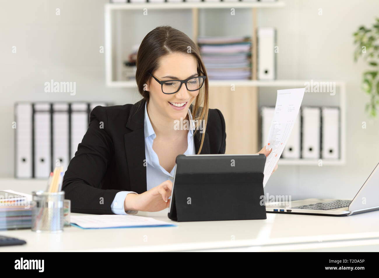 Felice lavoratore di ufficio lavora confrontando i documenti su carta online su un tablet Foto Stock
