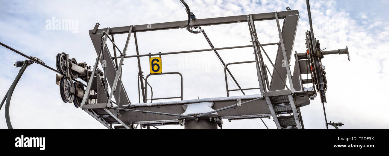 Funi di acciaio su ruote in meccanismo sulla parte superiore della seggiovia di sci colonna di supporto, numero 6 sulla piastra di giallo, cielo luminoso sfondo, ampia banner. Foto Stock