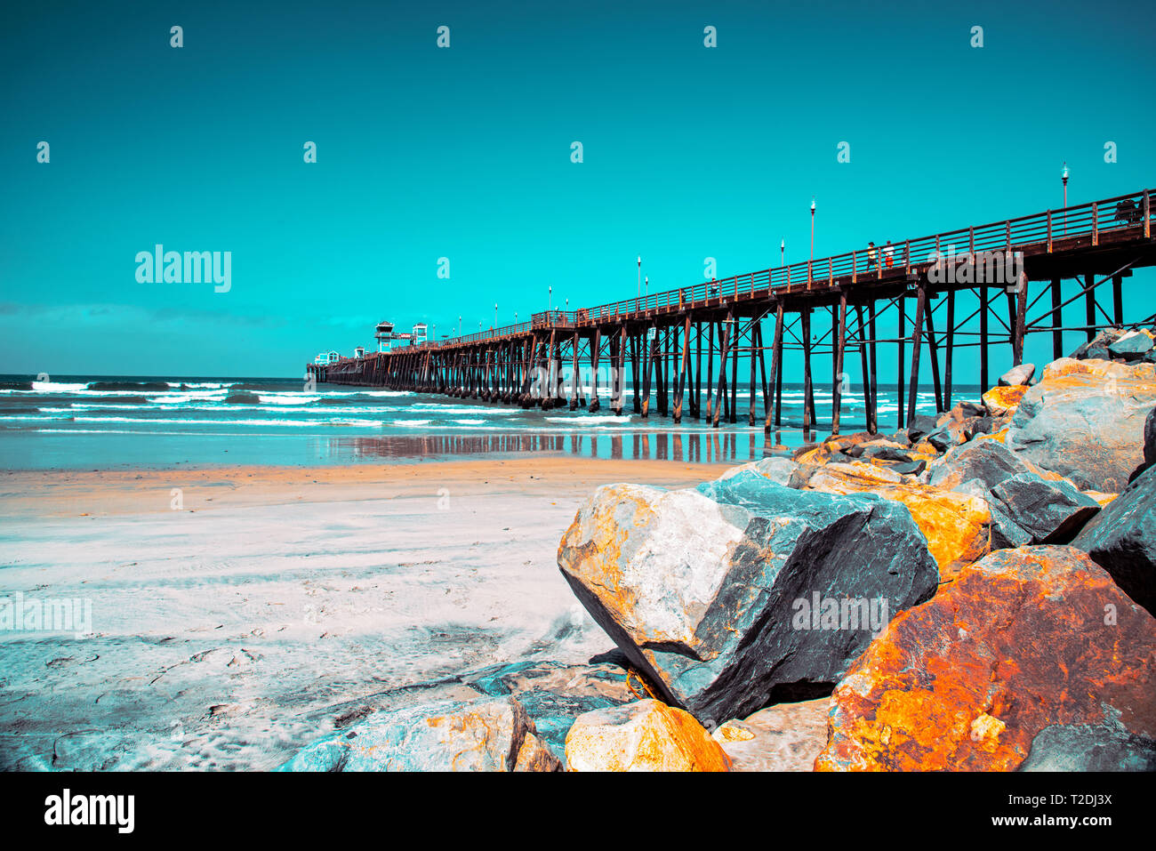 Grandi massi sulla spiaggia sabbiosa con vista oceano onde che si infrangono sotto il luminoso cielo blu. Foto Stock