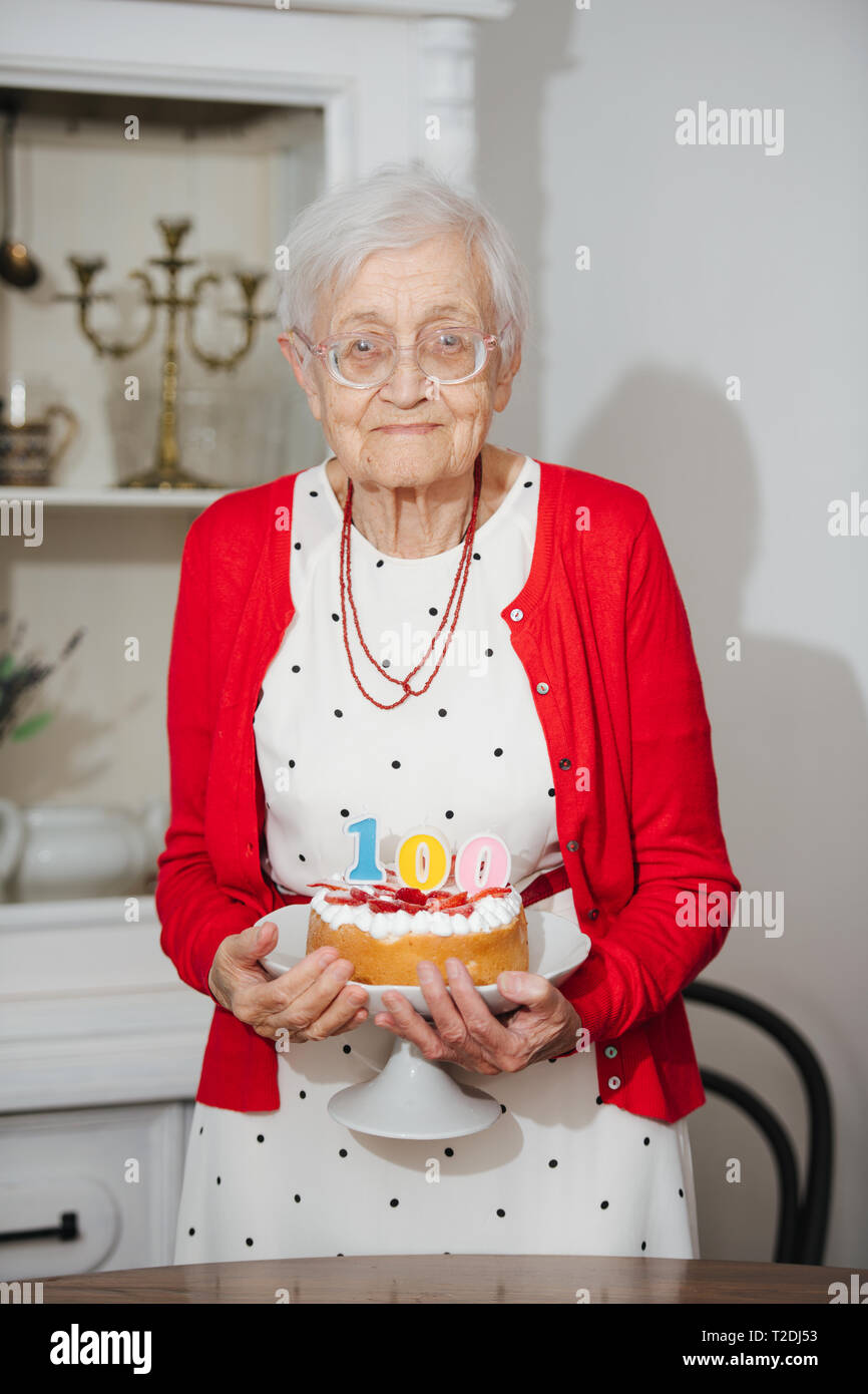 Senior felice ben vestito grigio donna dai capelli festeggia il suo centesimo compleanno a casa. Foto Stock