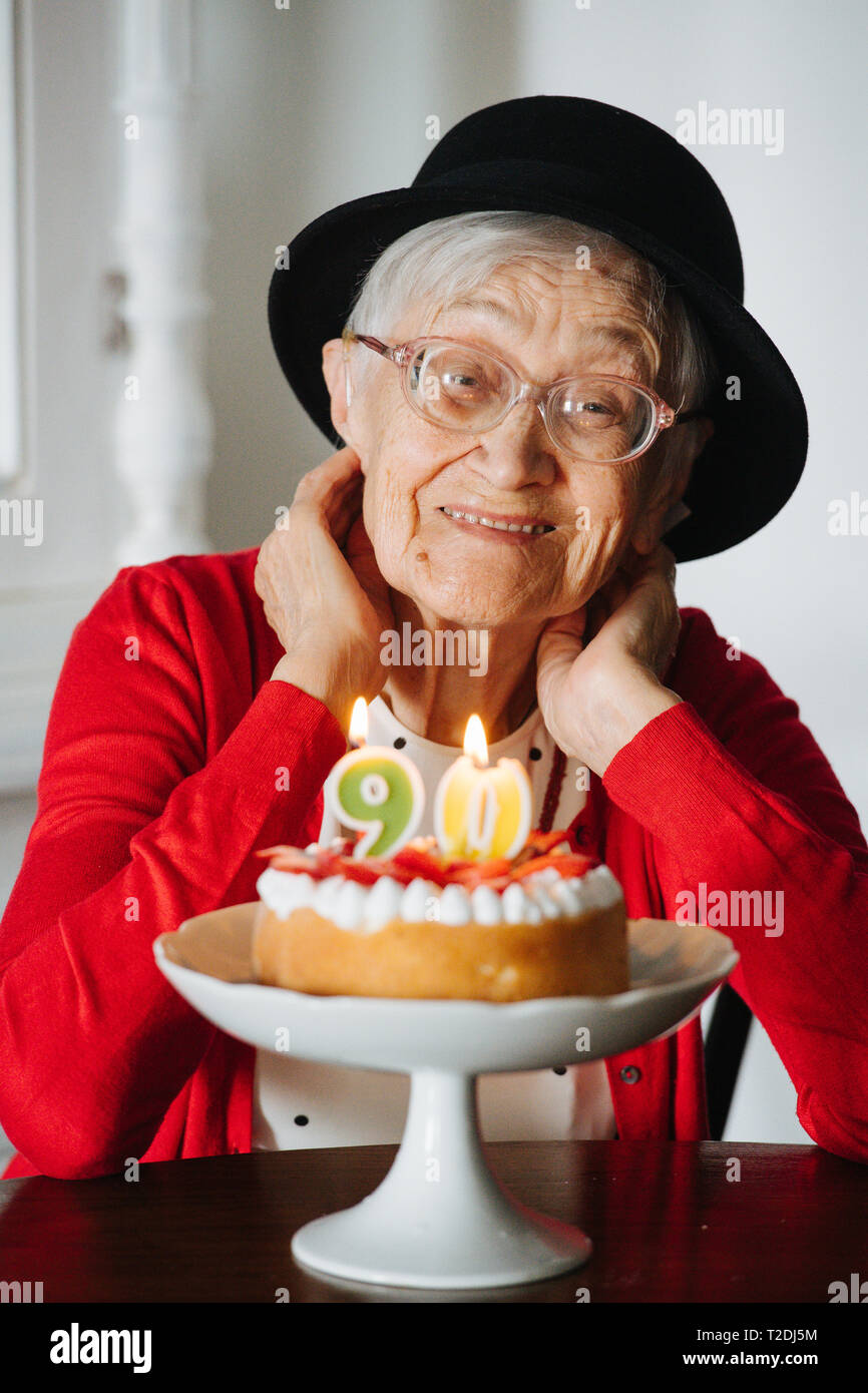 Senior felice ben vestita di nero mini hat grigio donna dai capelli festeggia il suo novantesimo compleanno a casa. Foto Stock