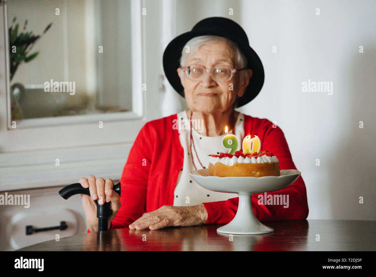 Rispettabile ben vestita di nero mini hat dai capelli grigi donna senior con canna celebra il suo novantesimo compleanno a cena a casa. Foto Stock