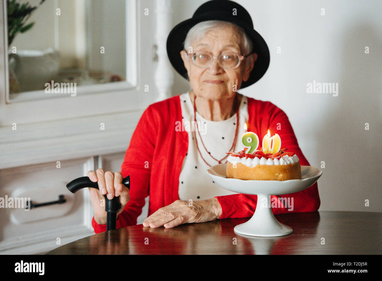 Rispettabile ben vestita di nero mini hat dai capelli grigi donna senior con canna celebra il suo novantesimo compleanno a cena a casa. Foto Stock