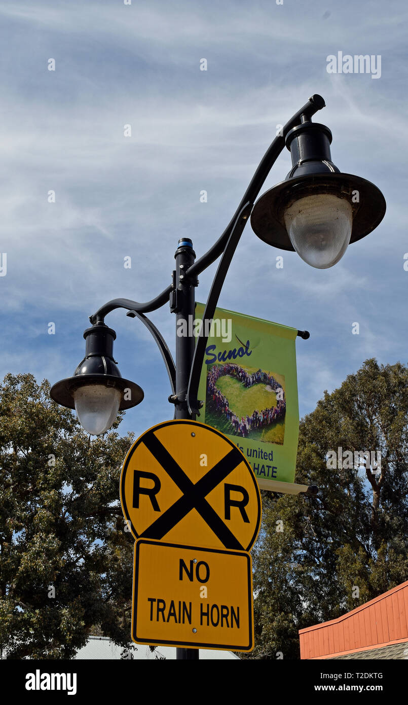 Sunol si erge contro l'odio banner e attraversamento ferroviario e nessun treno horn indicazioni su un palo della luce in California Foto Stock