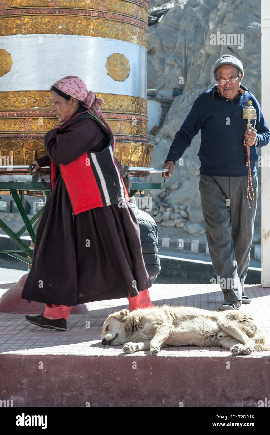 Un buddista uomo e donna con ruota di preghiera e la preghiera di perline in mano, a piedi intorno ad un enorme oro ruota di preghiera in Leh-Ladakh. India Foto Stock