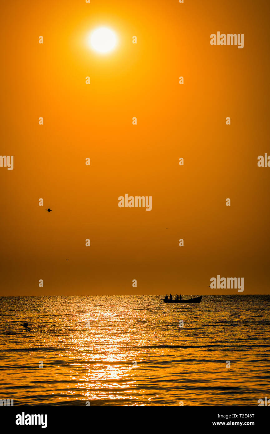 Sagome dei pescatori in mare su una barca da pesca al mattino con gli uccelli volare sopra il mare e il sole sul cielo Foto Stock