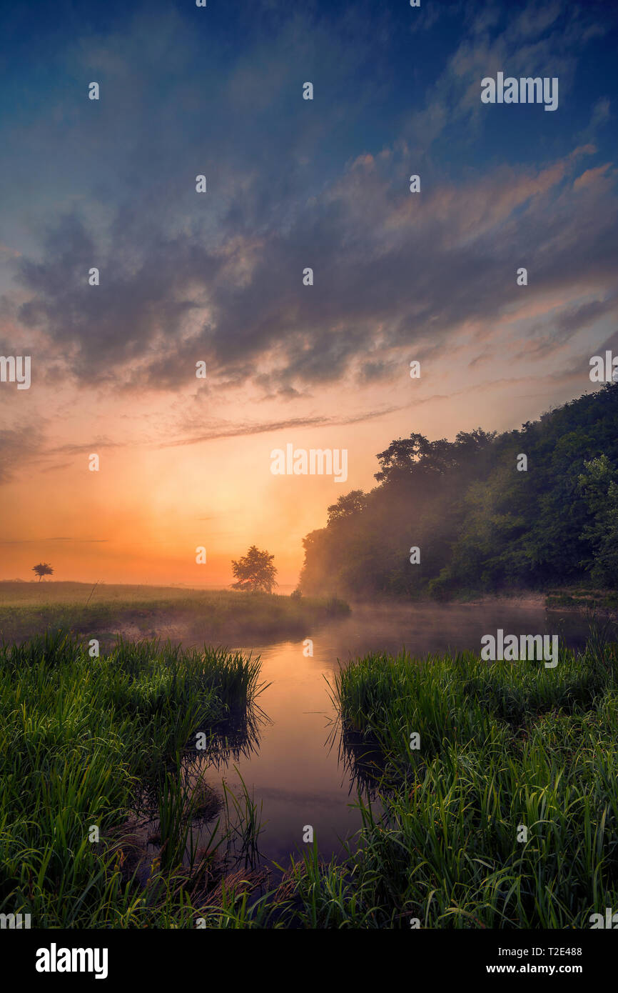 Bel mattino su un meandro del fiume in un paesaggio naturale con un sacco di nebbia e vapore a sunrise e drammatici nuvole contro un cielo blu Foto Stock