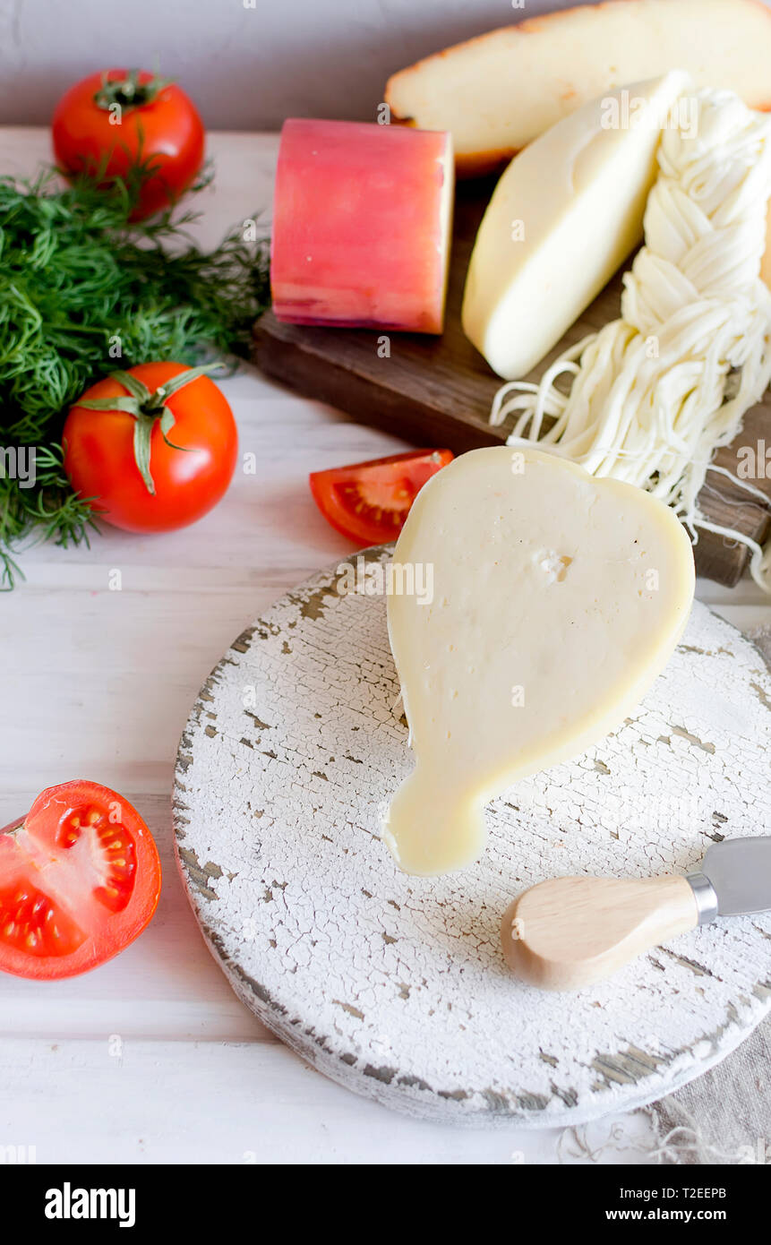 Un assortimento di dolci formaggi in varie forme e dimensioni su sfondo di legno, suluguni, spiralina, Cacocavallo con pomodori e basilico Foto Stock