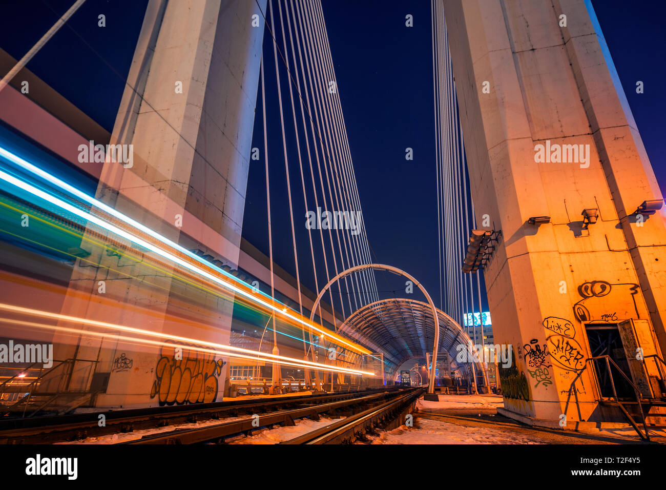 Night Shot con esposizione lunga con una fermata del tram che passa da e lasciare striature chiare e due rotaie utilizzato dal tram per il trasporto pubblico che passa su un mod Foto Stock