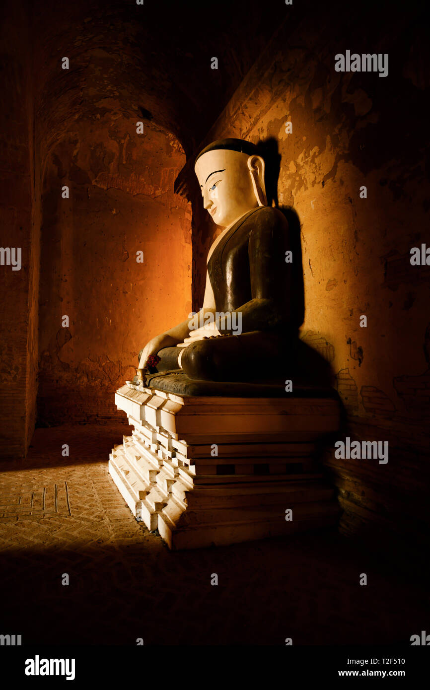 Statua del Buddha seduto in una piena posizione del loto illuminati dalla luce naturale del sole che filtra attraverso l'ingresso di un tempio di Bagan. Foto Stock