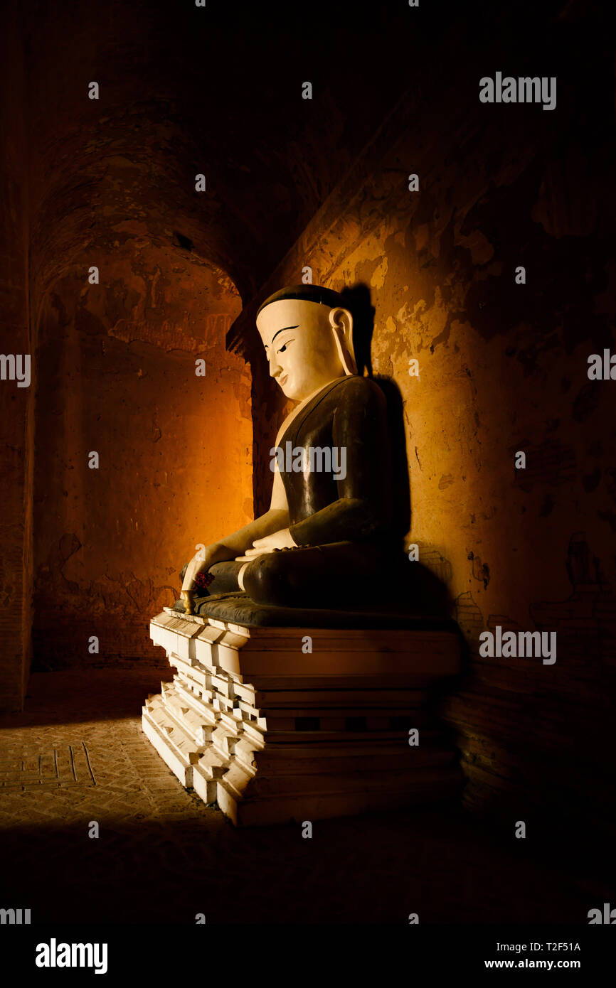 Statua del Buddha seduto in una piena posizione del loto illuminati dalla luce naturale del sole che filtra attraverso l'ingresso di un tempio di Bagan. Foto Stock