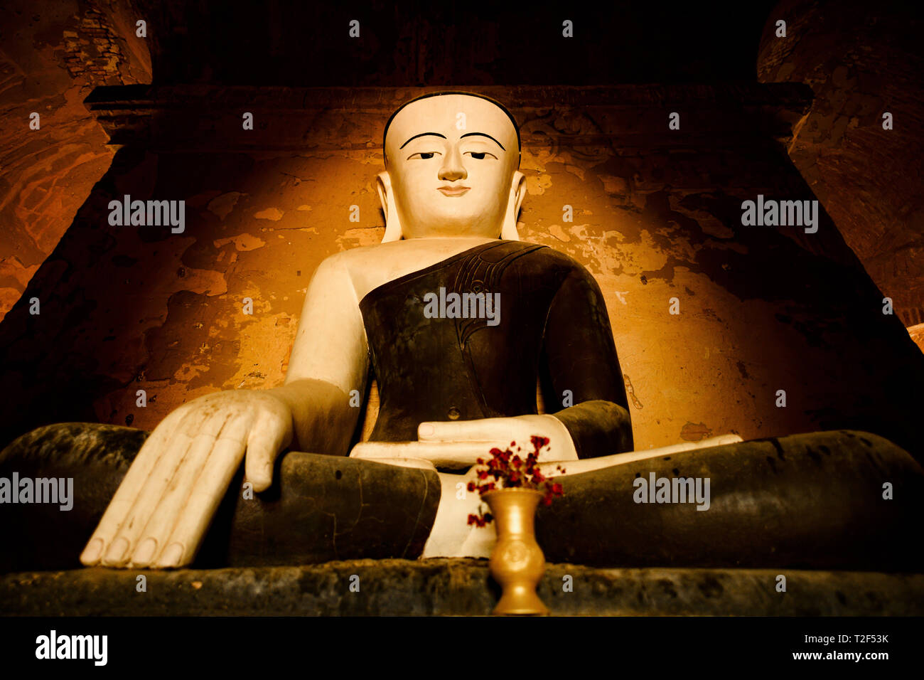 Statua del Buddha seduto in una piena posizione del loto illuminati dalla luce naturale del sole che filtra attraverso l'ingresso di un tempio di Bagan. Foto Stock