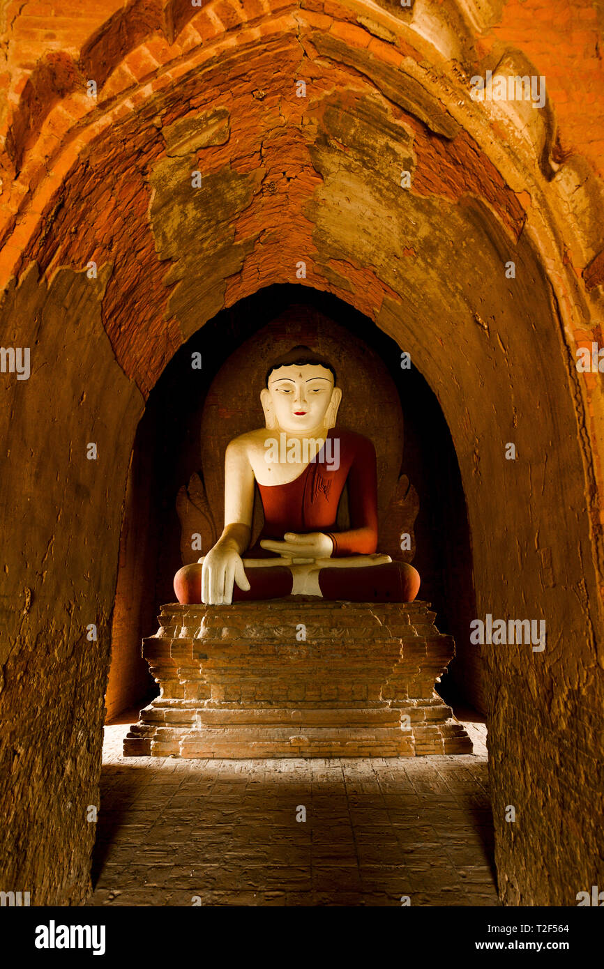 Statua del Buddha seduto in una piena posizione del loto illuminati dalla luce naturale del sole che filtra attraverso l'ingresso di un tempio di Bagan. Foto Stock