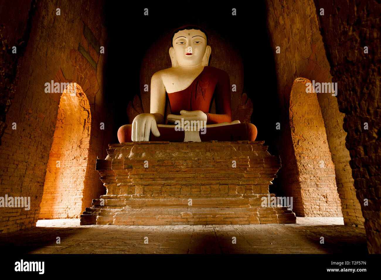 Statua del Buddha seduto in una piena posizione del loto illuminati dalla luce naturale del sole che filtra attraverso l'ingresso di un tempio di Bagan. Foto Stock