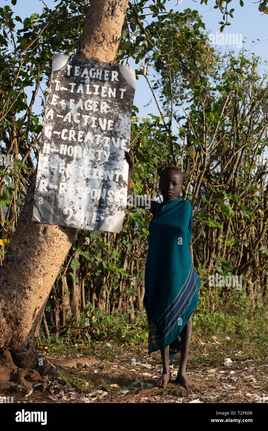 Uno scolaro sorge nella parte anteriore di un segno a una scuola nella valle dell'Omo Etiopia. Foto Stock