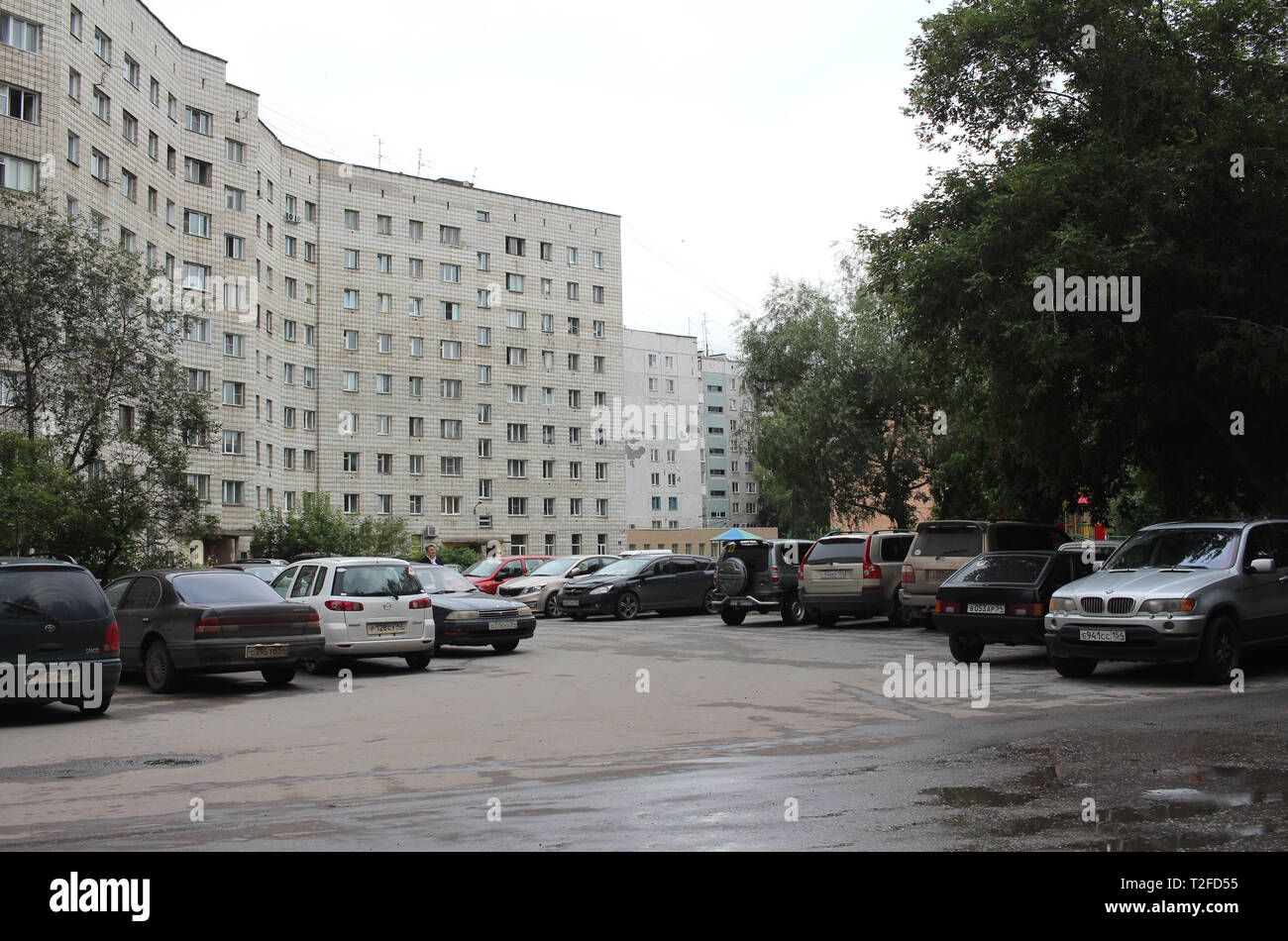 Nuvoloso cantiere di pietra Novosibirsk street sorge a più piani edificio residenziale ingombra con sporco auto nel parcheggio Foto Stock