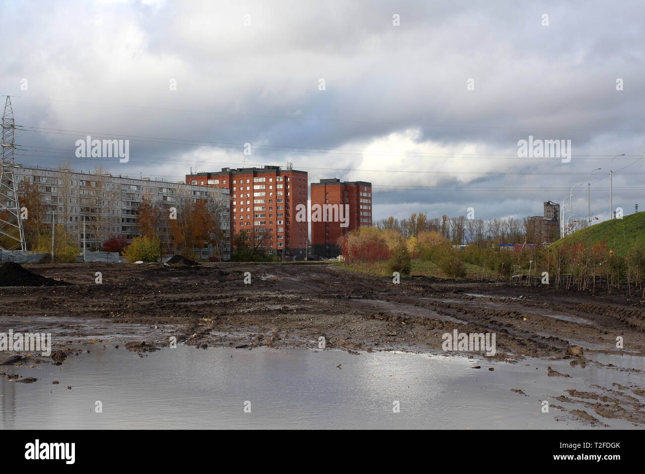 Una grande pozzanghera sporca sulla strada di fronte ad un nuovo complesso residenziale in costruzione di case in mattoni di nuovi edifici in autunno a Novosibirs Foto Stock
