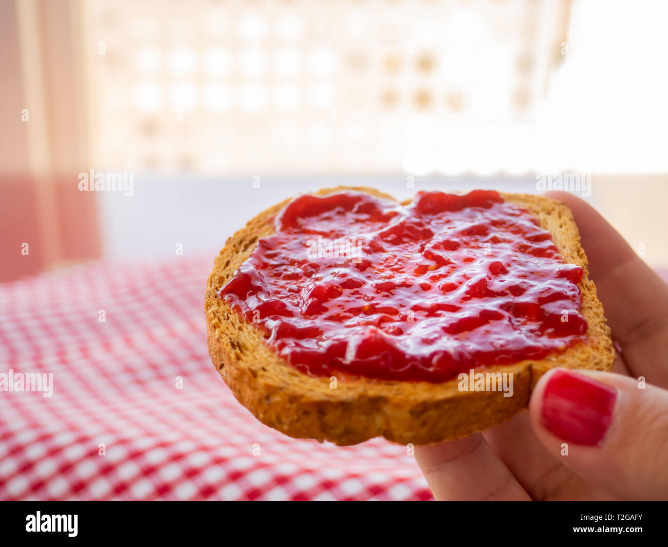 Una donna con le unghie dipinte di rosso con una fetta di pane tostato in mano con confettura di lamponi Foto Stock