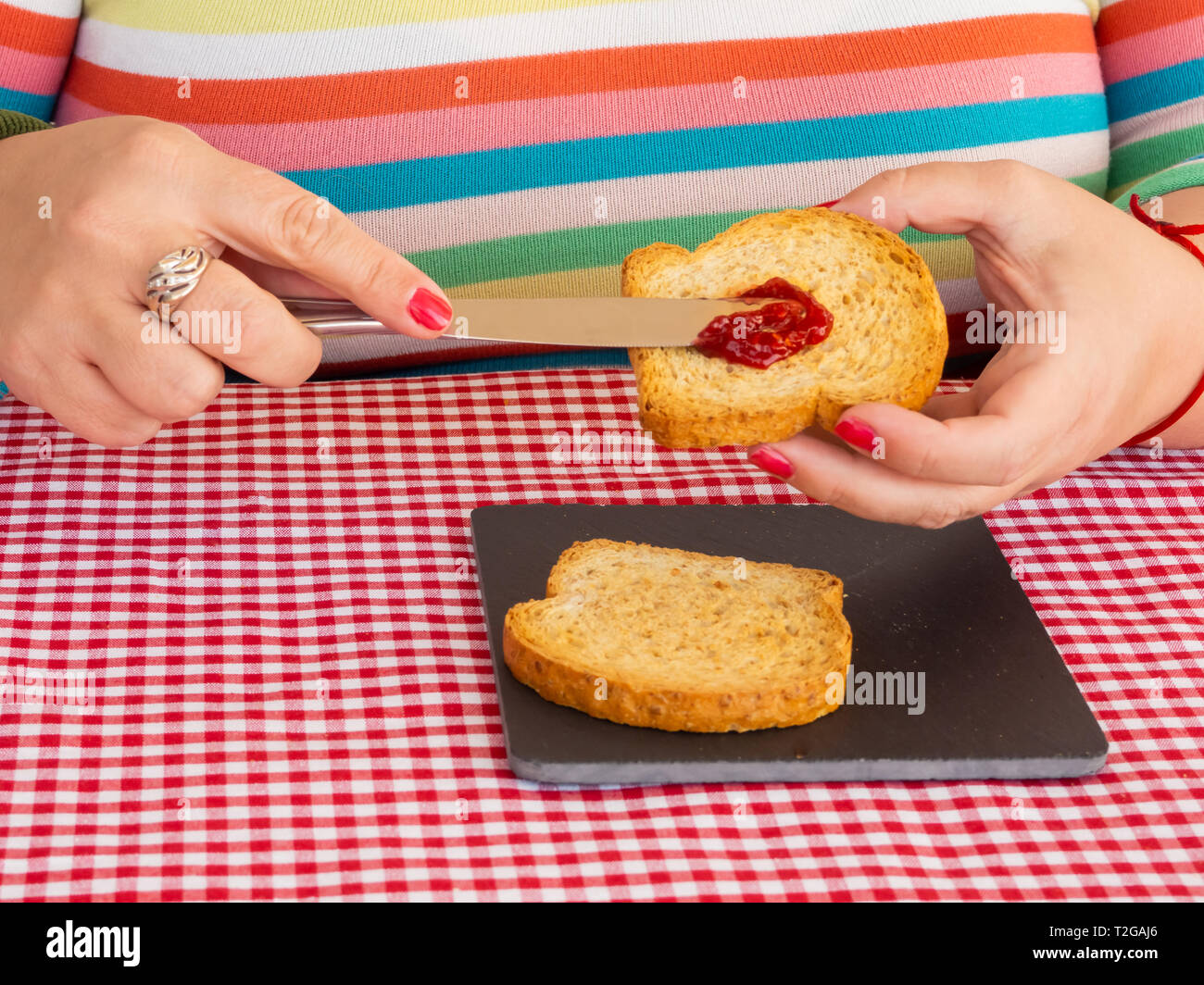 Una donna con unghie dipinte di rosso di spalmatura di marmellata di lamponi con un coltello su una fetta di pane tostato Foto Stock