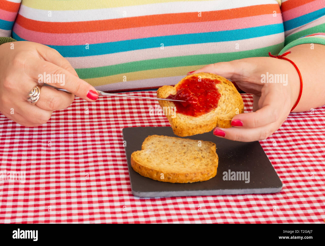 Una donna con unghie dipinte di rosso di spalmatura di marmellata di lamponi con un coltello su una fetta di pane tostato Foto Stock