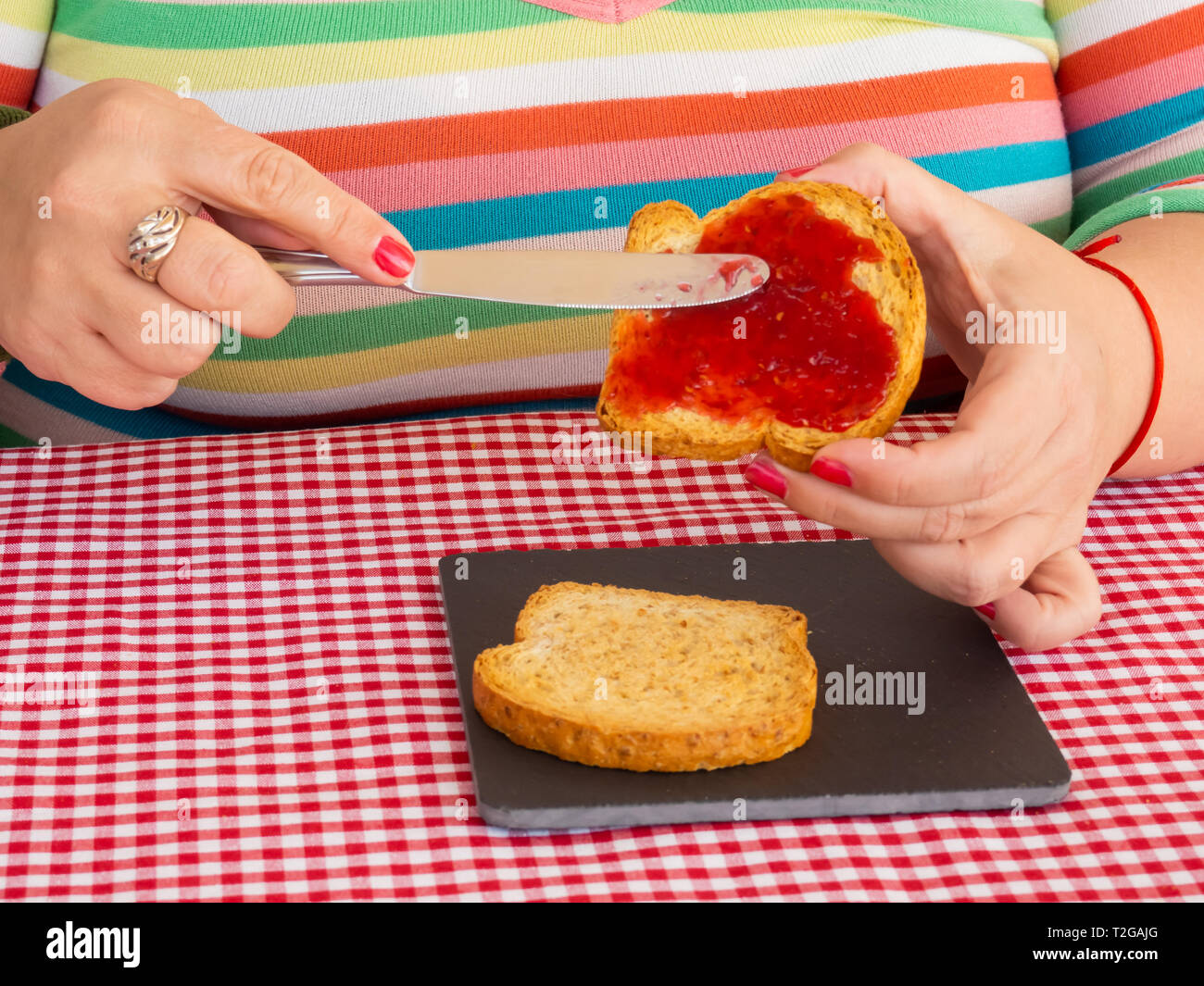 Una donna con unghie dipinte di rosso di spalmatura di marmellata di lamponi con un coltello su una fetta di pane tostato Foto Stock