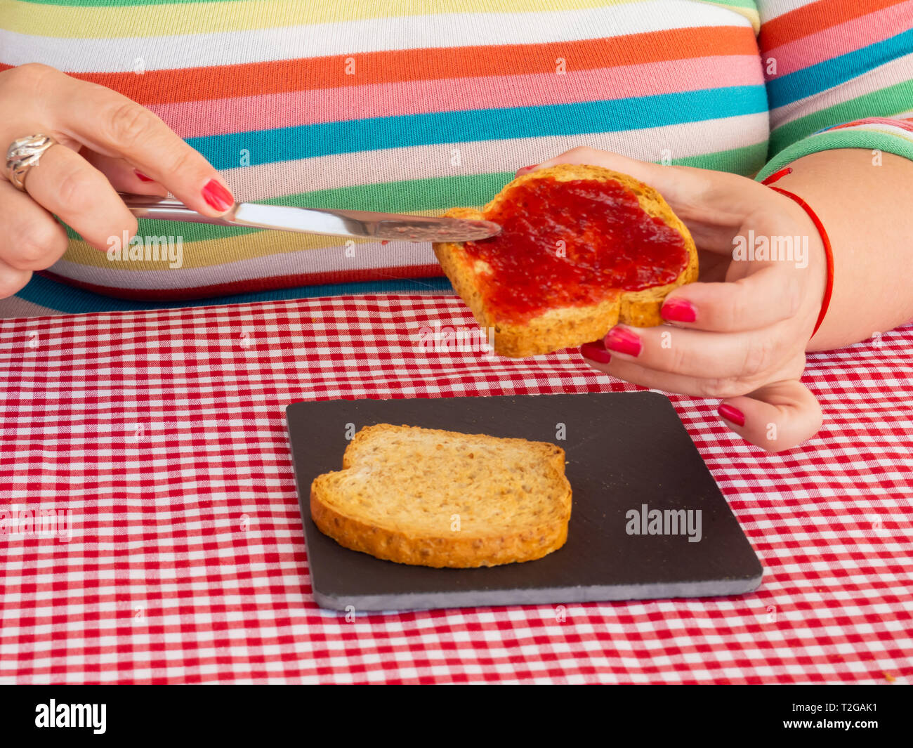 Una donna con unghie dipinte di rosso di spalmatura di marmellata di lamponi con un coltello su una fetta di pane tostato Foto Stock