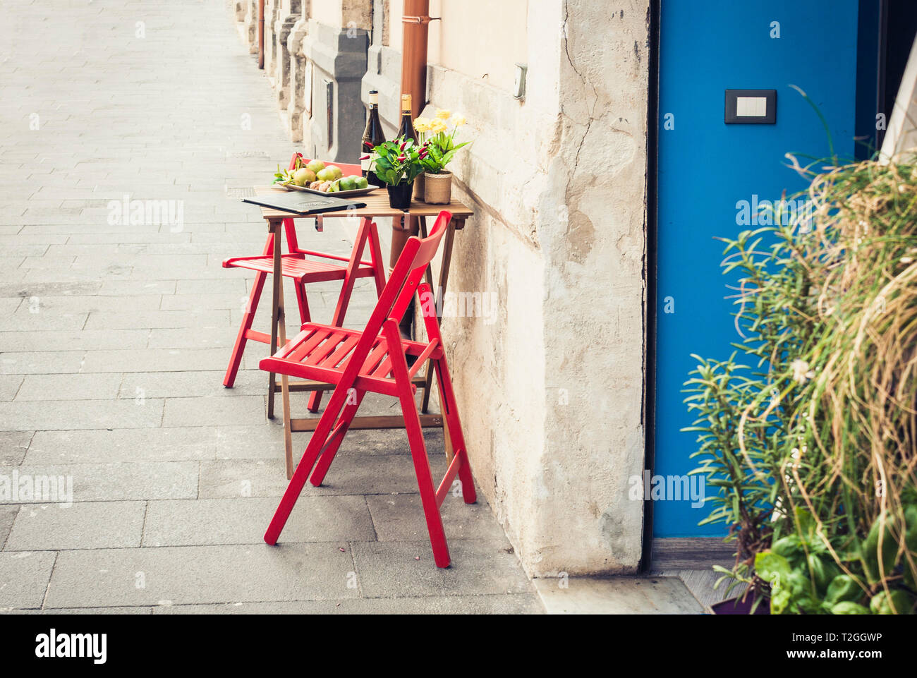 Red tavolo e sedia in una caffetteria all'aperto con blue porta in legno di Siracusa (Siracusa) Sicilia Foto Stock