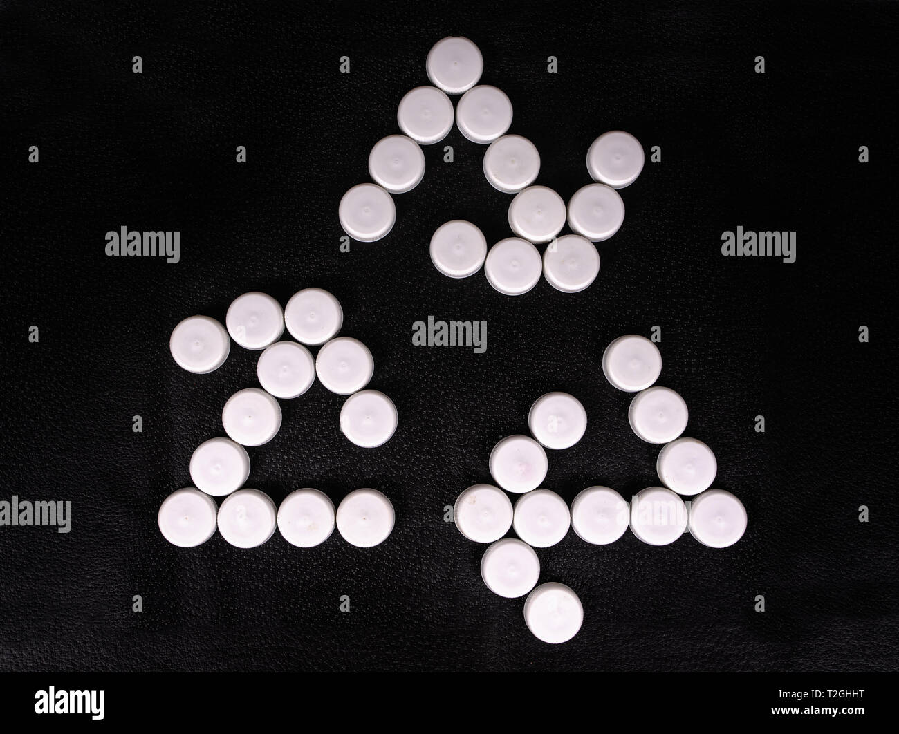 Simbolo di riciclaggio realizzato con bottiglie di plastica tappi su una superficie nera Foto Stock
