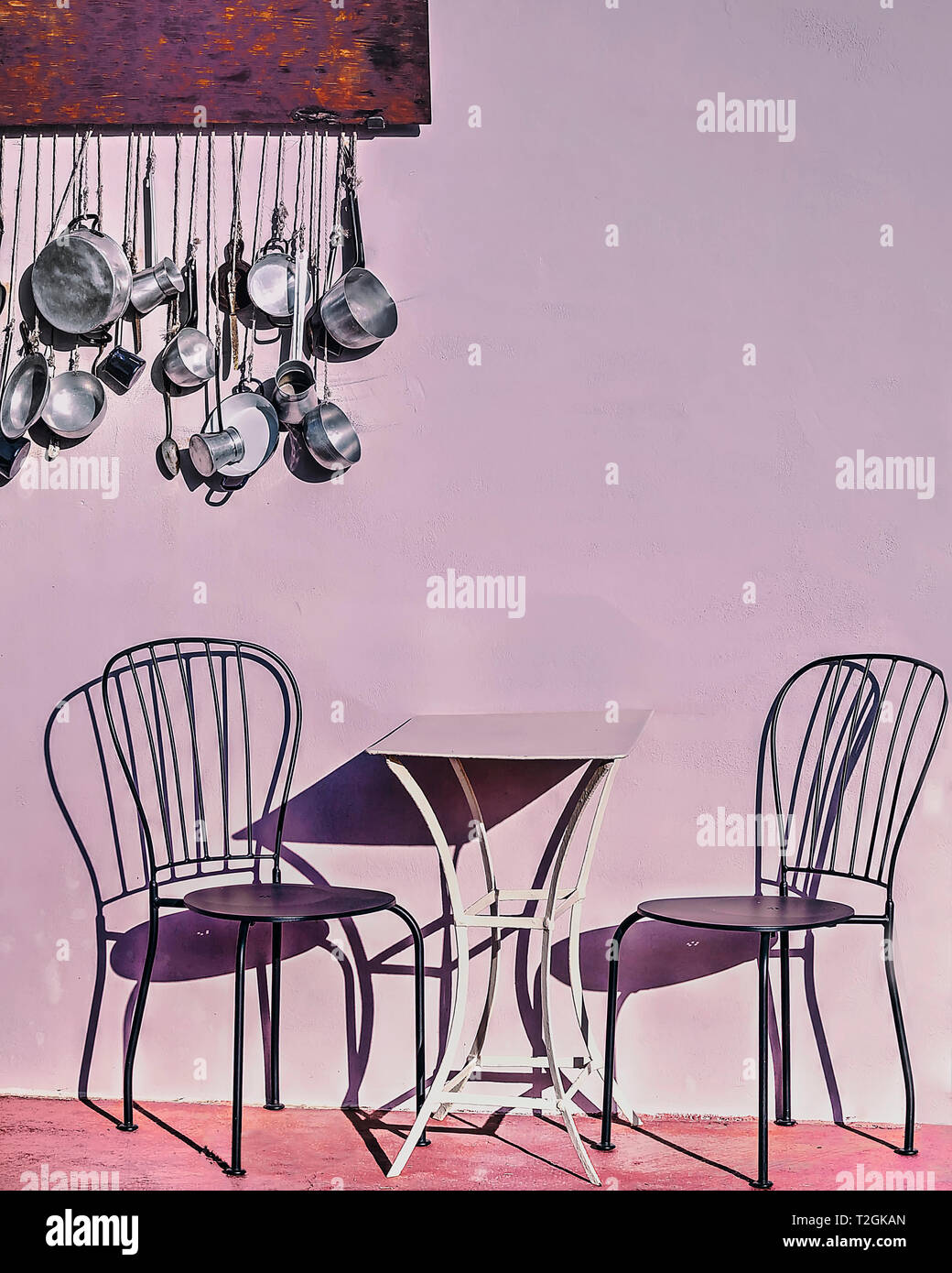 Un tavolo e due sedie all'aperto con le ombre . Cucina pentole e padelle appesi in background. Immagine di stock Foto Stock
